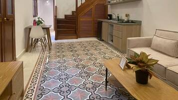 A spacious living area with a patterned floor, a staircase to an upper level, a kitchen area, and a seating area with a plant.