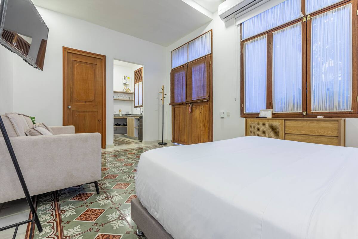 A hotel room with a bed, a sofa, a wooden wardrobe, a mirror, and a window with curtains.