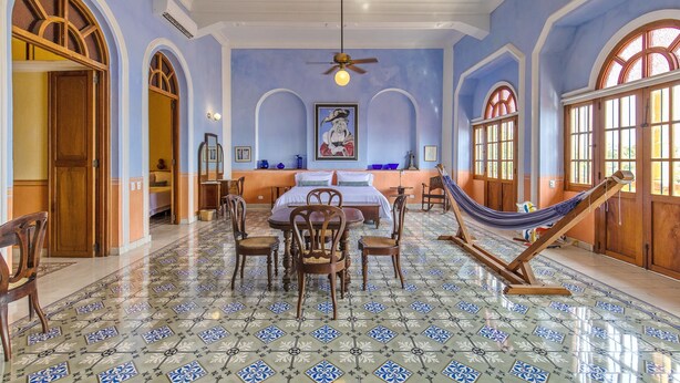 A spacious room with a large bed, a dining table with chairs, a hammock, and a ceiling fan.