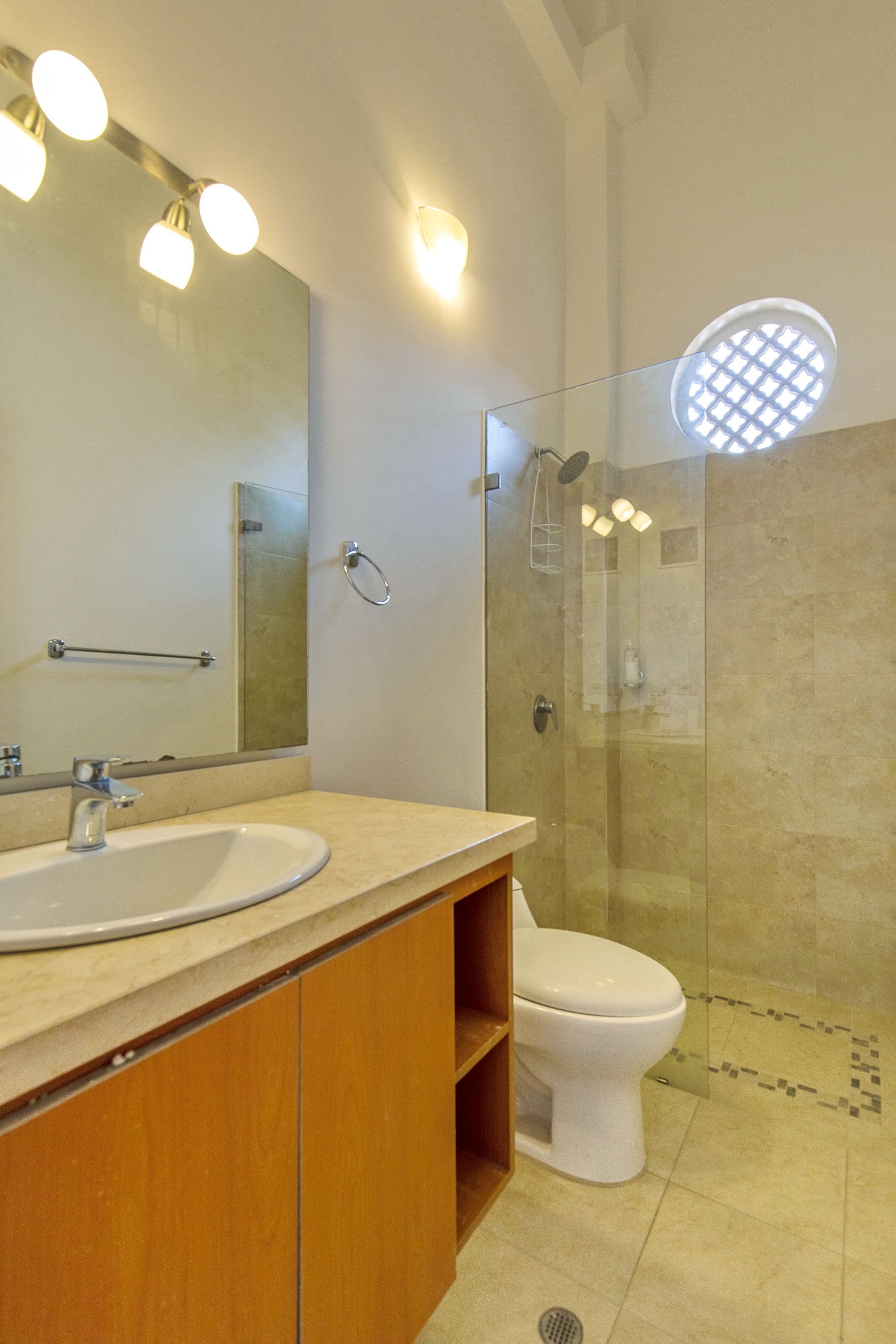 A bathroom with a sink, mirror, toilet, and glass-enclosed shower.