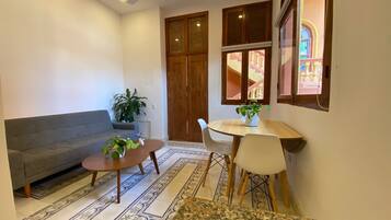 Una sala de estar con un sofá gris, una mesa de centro, una mesa de comedor con sillas y una planta grande en maceta.