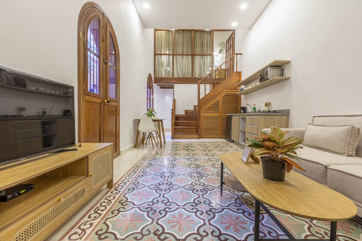 A modern living room with a TV, wooden furniture, a staircase, and a kitchen area.