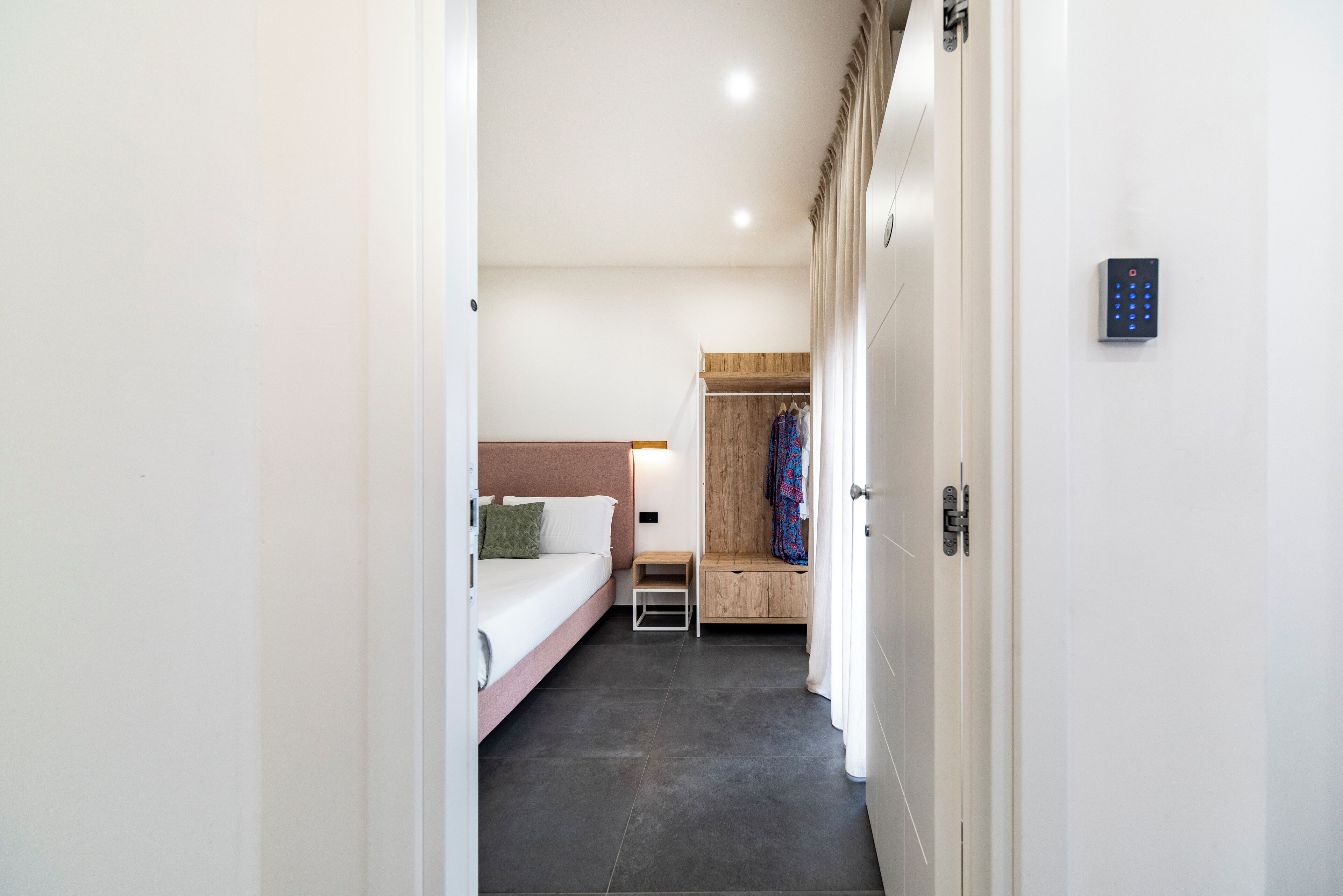 Une chambre d’hôtel moderne avec un lit, une table de chevet et un banc en bois où sont posés des vêtements.