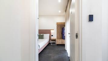 Une chambre d’hôtel moderne avec un lit, une table de chevet et un banc en bois où sont posés des vêtements.