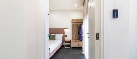 A modern hotel room with a bed, bedside table, and a wooden bench with clothes.