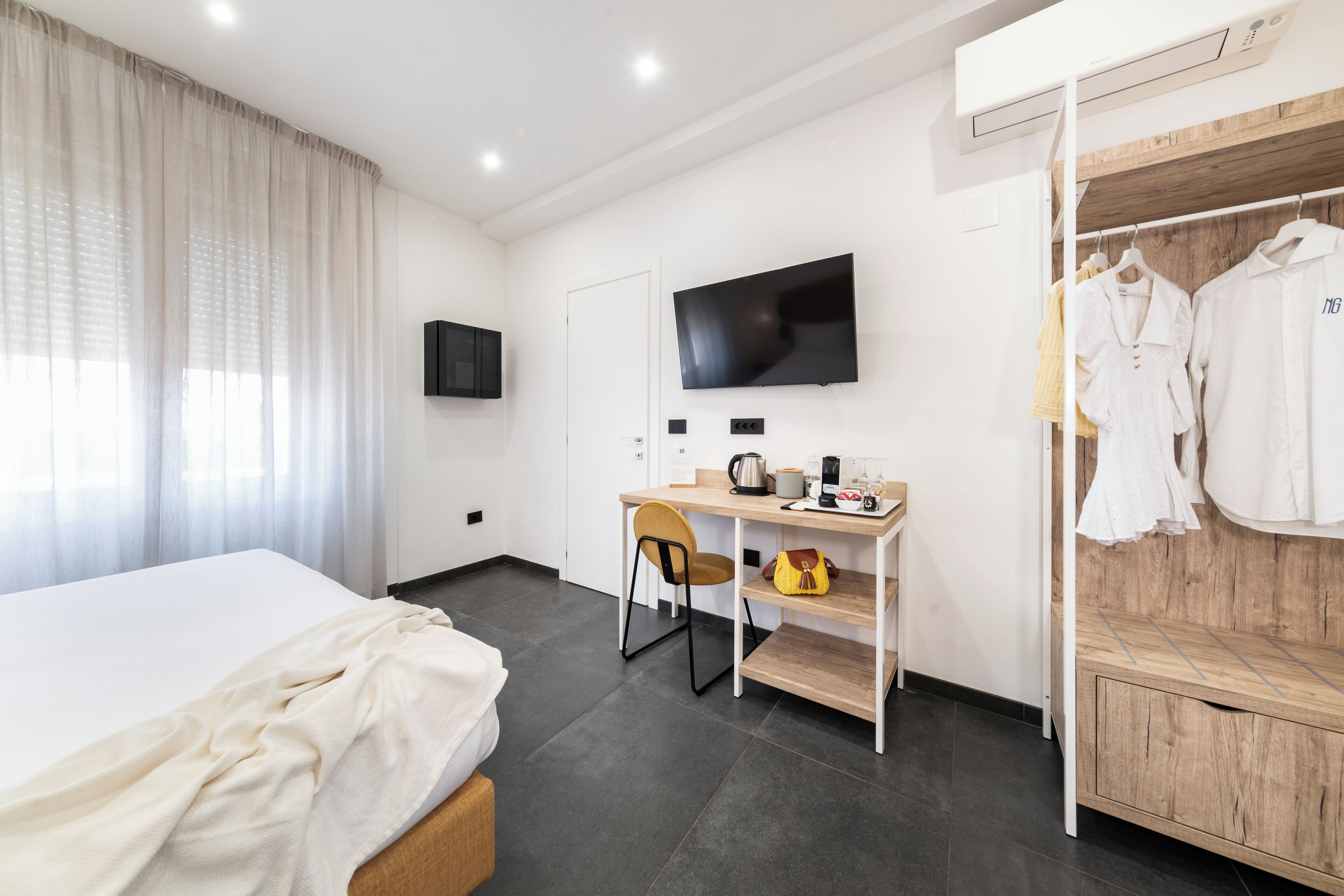 Une chambre d’hôtel comprenant un lit, un bureau avec une chaise, un téléviseur fixé au mur et une armoire contenant des vêtements.