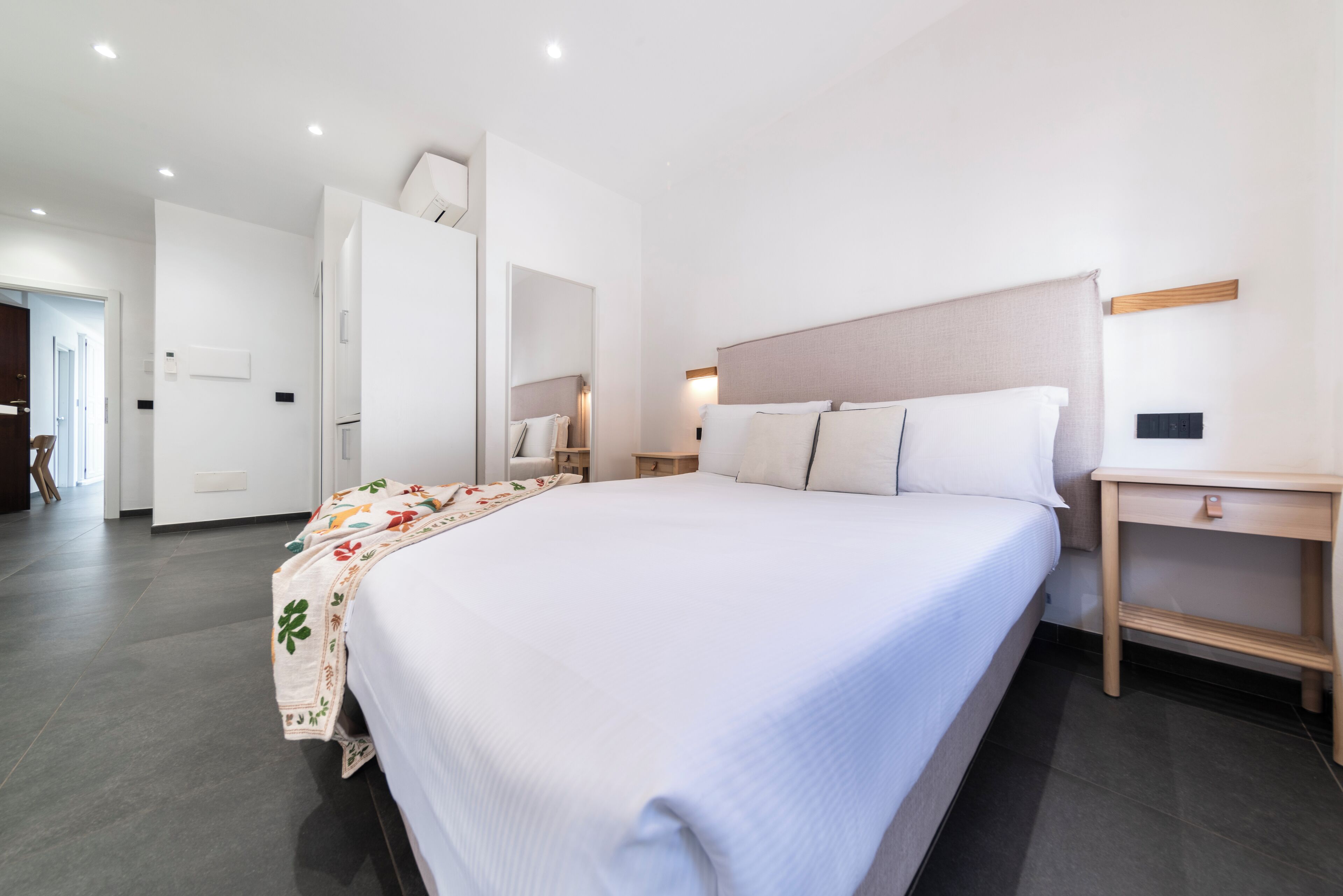 Una habitación de hotel moderna con una cama grande, mesitas de noche, un espejo y un armario.