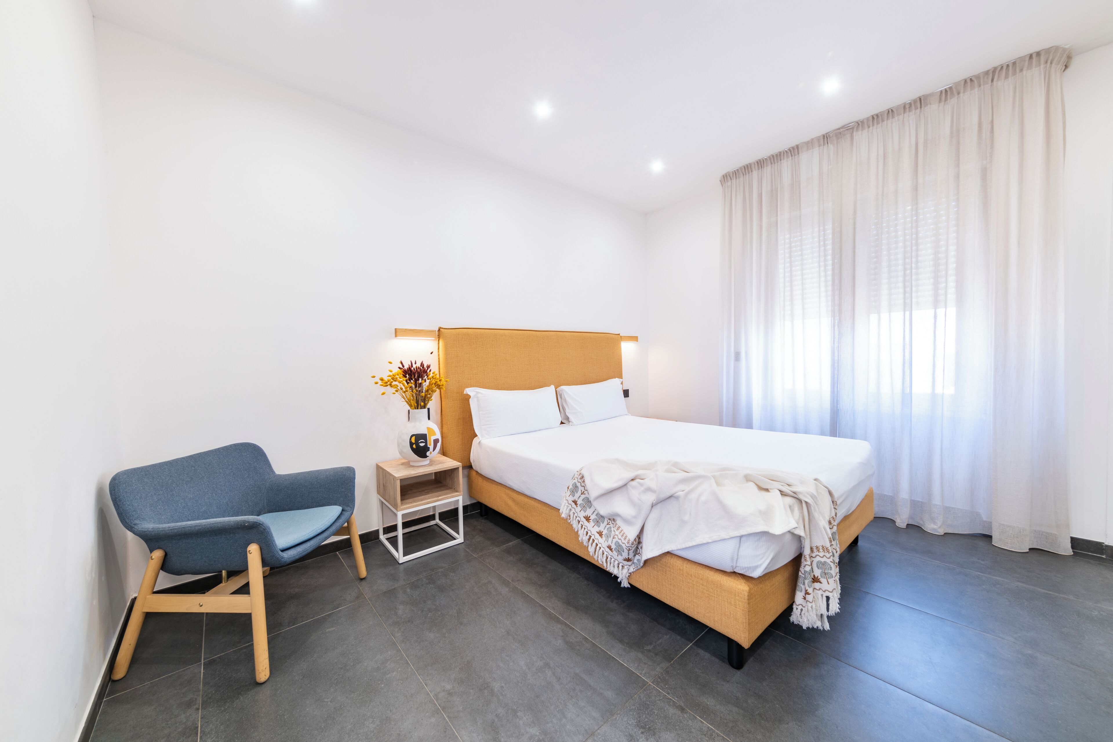 A hotel room with a bed, a chair, a nightstand, and a window with curtains.