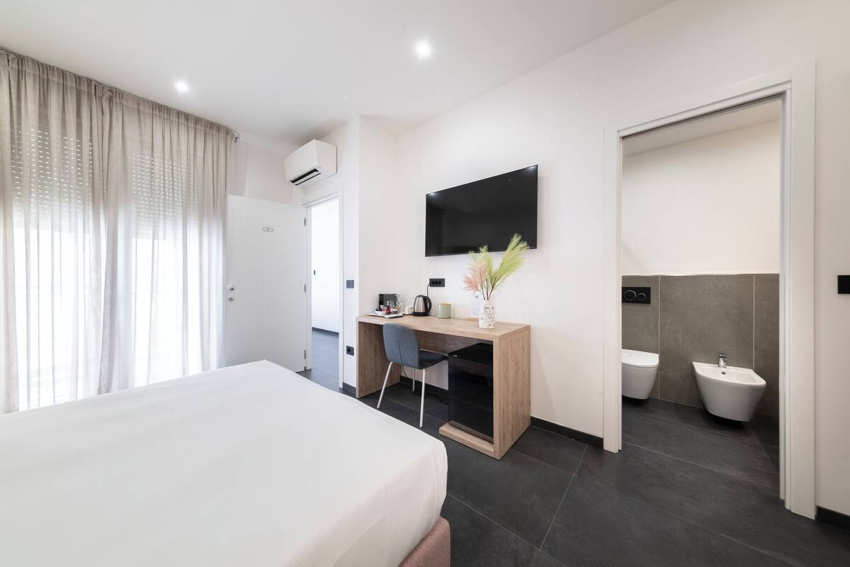 Une chambre d’hôtel moderne équipée d’un lit, d’un bureau avec une chaise, d’une télévision, de toilettes et d’un bidet.