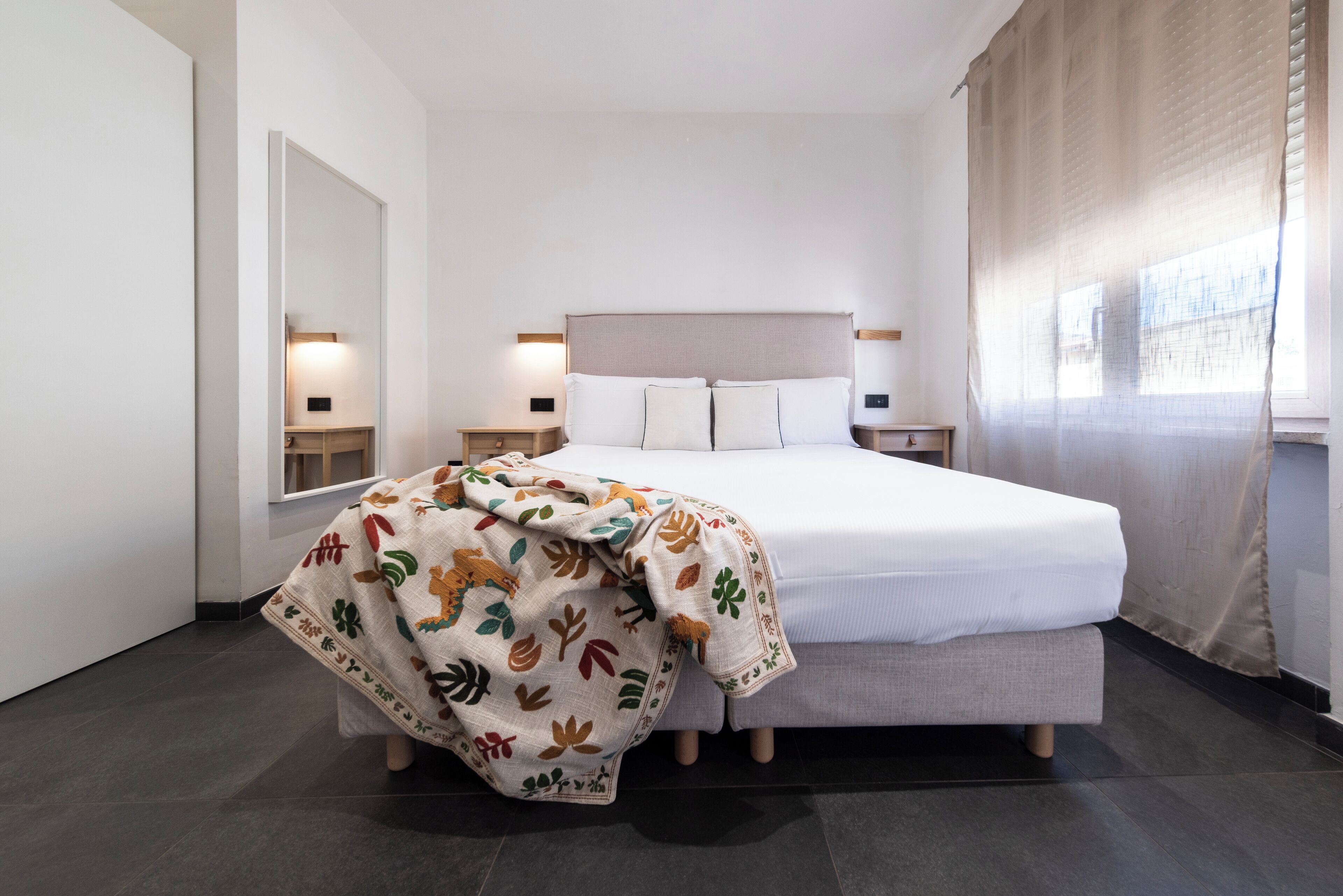 A hotel room with a large bed, bedside tables, a mirror, and a window with curtains.