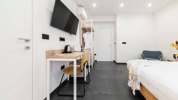 Ein modernes Hotelzimmer mit einem Holztisch, einem Flachbildfernseher, einem Bett mit weißer Bettdecke und einem blauen Sessel.