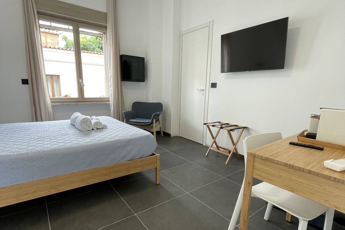 Une chambre à coucher comprenant un lit, un bureau, une chaise, un téléviseur et une fenêtre avec des rideaux.
