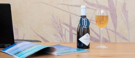 A bottle of wine and a glass on a wooden table with a laptop and a magazine.