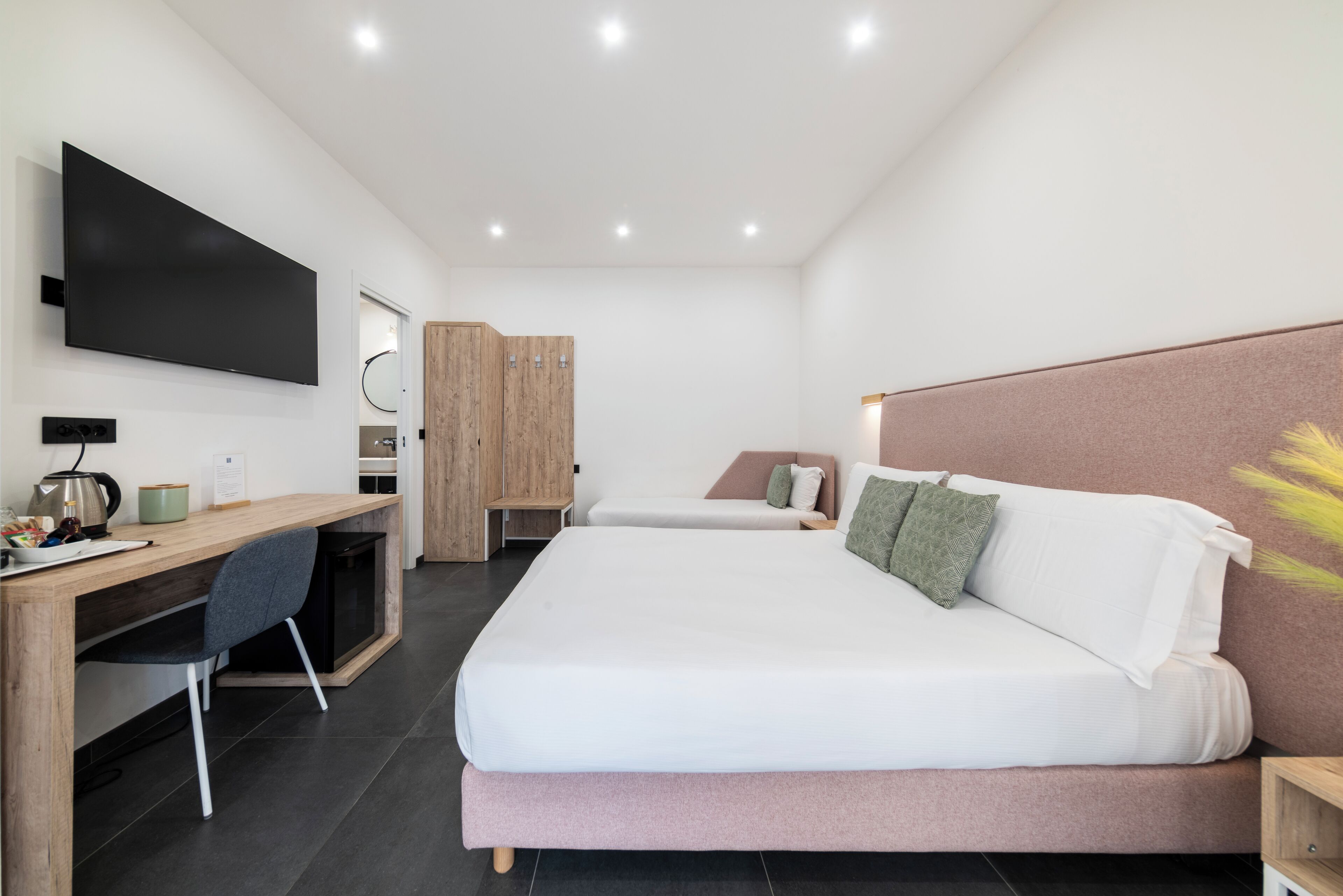 Una habitación de hotel moderna con una cama grande, un escritorio con una silla, un televisor y un armario.