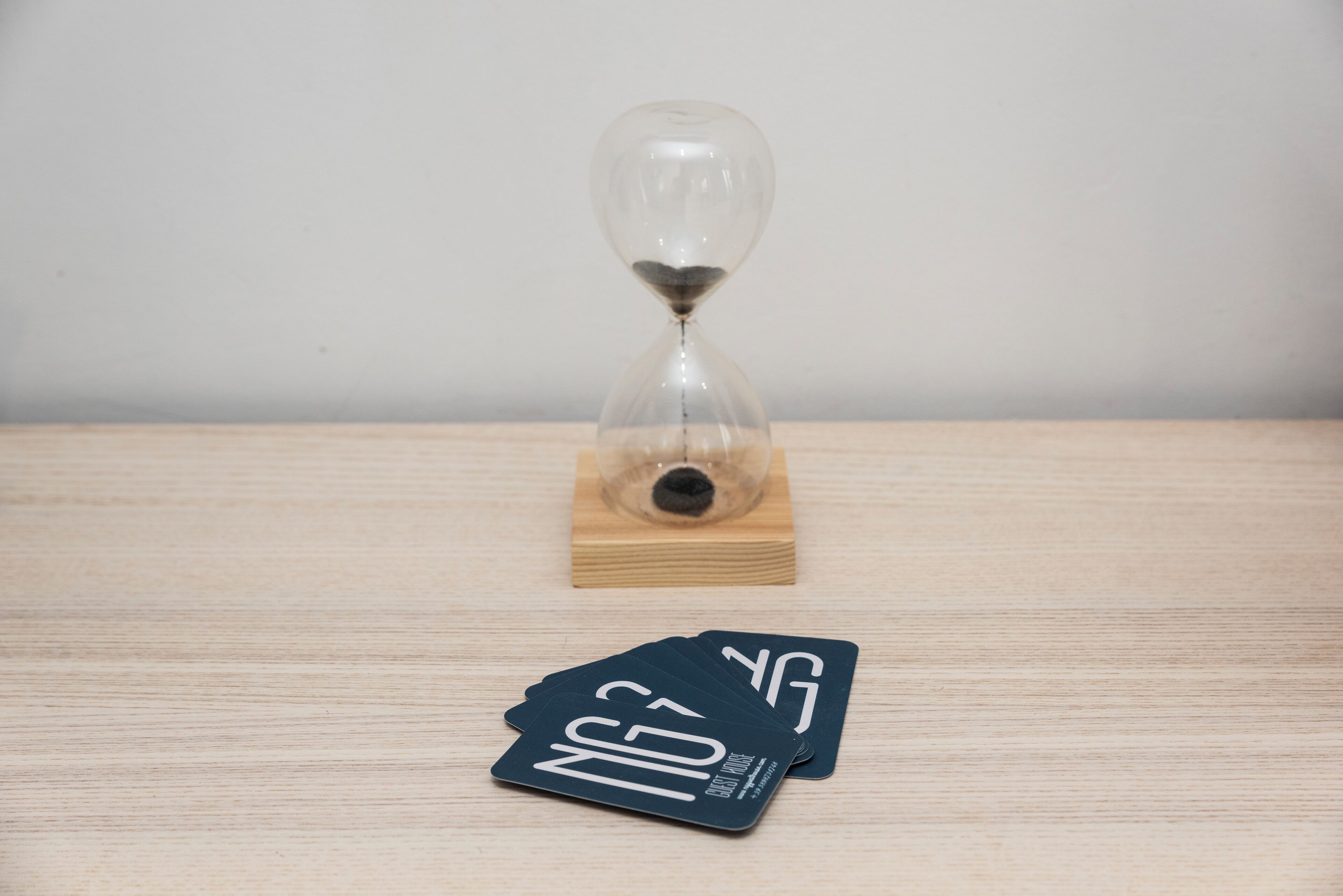 An hourglass on a wooden block with a pair of cards labeled "NG" in front of it.