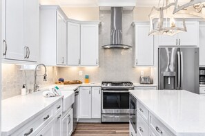 Una cocina moderna con armarios blancos, una campana extractora de acero inoxidable, un horno empotrado y un refrigerador.