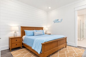 Un dormitorio con una cama de madera, dos mesitas de noche, un aplique de pared y una puerta de ducha de vidrio.