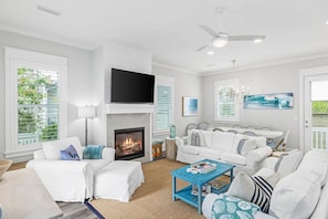 A spacious living room with a fireplace, white furniture, and large windows.