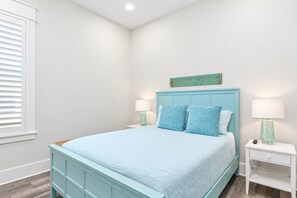 Un dormitorio con una cama, dos mesitas de noche, un letrero en la pared y una ventana con persianas.