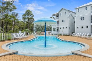 A swimming pool with a water fountain, surrounded by lounge chairs and a fence.