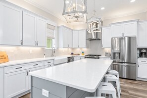 A modern kitchen with white cabinetry, a large island, stainless steel appliances, and pendant lighting.