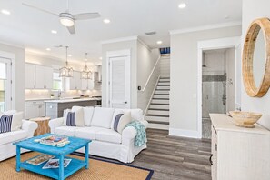 A modern interior with a white sofa, blue coffee table, and a kitchen area with white cabinets and pendant lighting.
