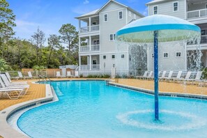 Una piscina con fuente, rodeada de sillones de descanso y un edificio de varios pisos con balcones.