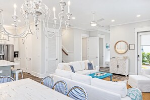 Una sala de estar moderna con un sofá blanco, sillas con estampado azul, una mesa de comedor de madera y una araña.