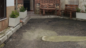 A courtyard with a gravel ground, a wooden bench, and a stone bench. There are two white planters with plants. A brick wall surrounds the courtyard, and a door with a metal gate is visible. - RURAL HOUSE  (Yebra)