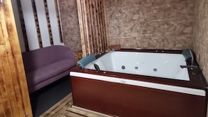 A room with a wooden floor, a purple sofa, a white bathtub, and a stone wall. - RURAL HOUSE  (Yebra)