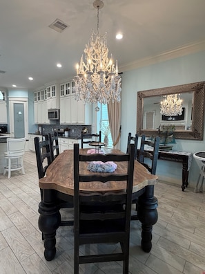 Uma sala de jantar com uma mesa de madeira, cadeiras, um candelabro e um espelho grande.
