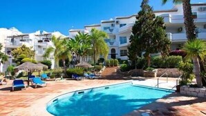 A swimming pool surrounded by lounge chairs and palm trees, with a building in the background. - Stylish one bed apartment at Matchroom CountryClub (Las Lagunas de Mijas)