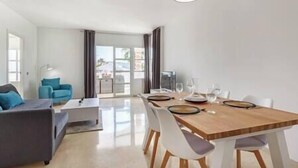 A modern living room with a dining area, featuring a wooden dining table, white chairs, and a grey sofa. - Stylish one bed apartment at Matchroom CountryClub (Las Lagunas de Mijas)