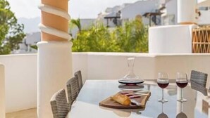A table with a glass of red wine, a plate with food, and a wine glass on a balcony with a view of buildings and greenery. - Stylish one bed apartment at Matchroom CountryClub (Las Lagunas de Mijas)