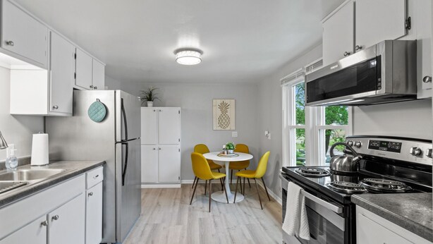 Una cocina moderna con armarios blancos, un refrigerador de acero inoxidable, una estufa y un comedor con sillas amarillas.