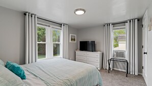 Un dormitorio con cama, cómoda, televisor y ventana con cortinas.