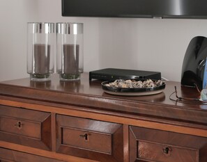 A wooden dresser with two clear glass vases, a black electronic device, and a plate with dried flowers.