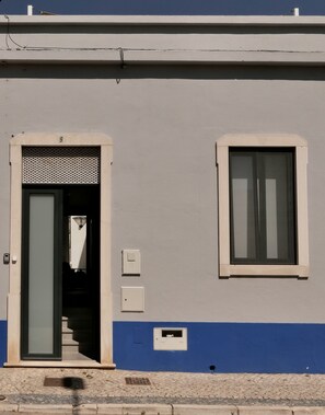 A building with a blue lower section, a white upper section, a door with a mesh grille, a window, and a small electrical box.