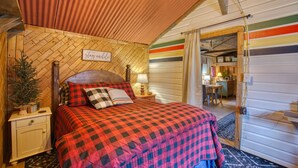 Une chambre confortable avec une couvre-lit à carreaux, une petite table de chevet avec une lampe et une pancarte sur laquelle on peut lire : « restez un peu ».