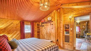 A cozy wooden room with a bed, a shelf with items, and a door leading to another room. - Vintage Riverside Cabin — Spacious Family Stay (Lyons)