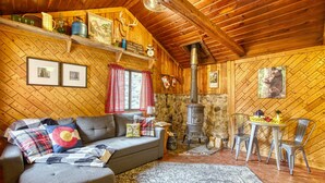 A cozy cabin interior with a fireplace, wooden walls, a sofa, and a dining area. - Vintage Riverside Cabin — Spacious Family Stay (Lyons)