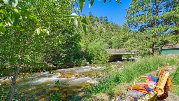 A river with a bridge, surrounded by greenery and a chair with a colorful blanket. - Vintage Riverside Cabin — Spacious Family Stay (Lyons)