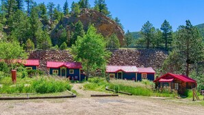 A rustic cabin area with multiple cabins, a large rock formation in the background, and a clear sky. - Vintage Riverside Cabin — Spacious Family Stay (Lyons)
