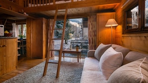 A cozy cabin interior with a wooden staircase, a sofa, and a dining area. - Mazot Les Tines, with hot tub (Chamonix-Mont-Blanc)