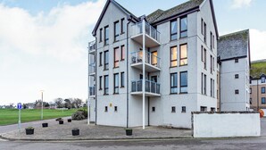Un immeuble moderne à plusieurs étages, doté de balcons, d’un toit plat et d’un espace extérieur pavé agrémenté de plantes en pot.
