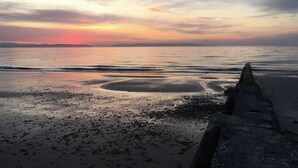 Une scène de plage avec un promontoire rocheux au premier plan et un coucher de soleil sur l’eau.