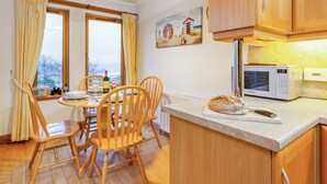 Une cuisine chaleureuse avec des meubles en bois, une table à manger entourée de chaises, une miche de pain et un tableau accroché au mur.