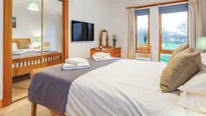 Une chambre d’hôtel avec un grand lit, une télévision, un miroir, une commode et une fenêtre avec des rideaux.