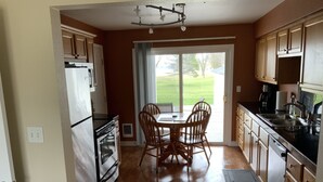 A kitchen with wooden cabinets, a dining table with chairs, a refrigerator, an oven, and a sink. - BEACHSIDE GETAWAY IN SHEBOYGAN (Sheboygan)