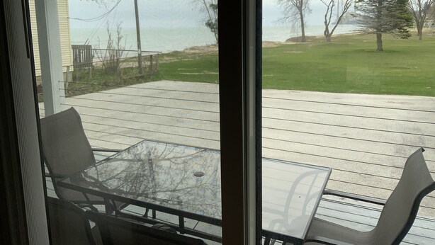 A patio with a glass table and chairs, overlooking a grassy area with trees and a building in the background. - BEACHSIDE GETAWAY IN SHEBOYGAN (Sheboygan)